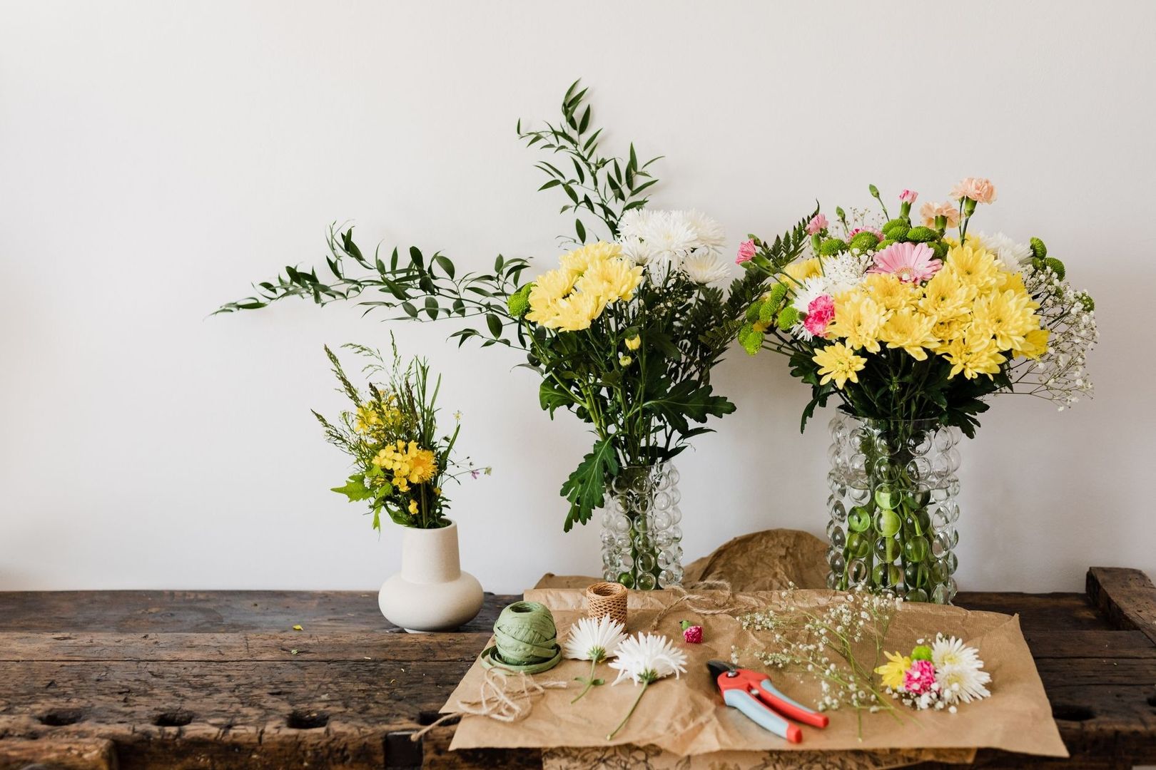 Tre vaser med färska blommor och verktyg för blomsterarbete